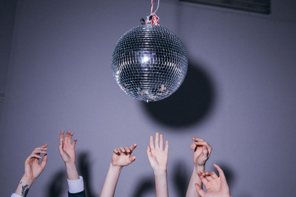 People reaching towards a disco ball creating a fun, light-hearted party vibe.